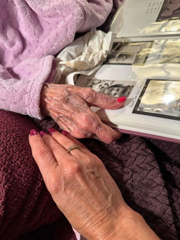 A younger hand holding an elderly hand while looking at old photographs in a scrapbook